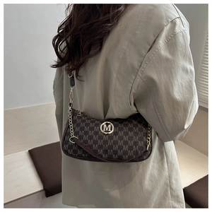 Detail of dark brown monogram shoulder bag with gold M logo on a minimalist background
