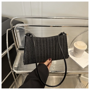 Dettaglio di una borsa a spalla nera intrecciata minimalista tenuta davanti a un scaffale