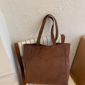 Detailed close-up of a dark brown suede tote bag resting on a wooden chair