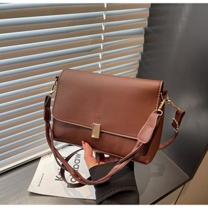 Close-up of a brown leather crossbody bag with a golden metal buckle and adjustable strap