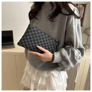 Detail view of a gray hand clutch with M-letter pattern and a convenient wrist strap