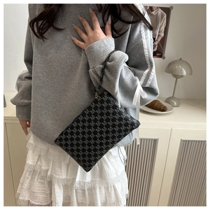 Detail of black clutch bag with grey letter pattern and wristlet held by a model