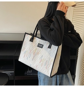 Detail of cream tote bag featuring colorful geometric embroidery and black leather handles