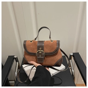 Close-up of brown suede crossbody bag with leather trim and large gold buckle detail