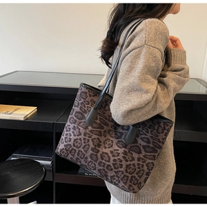 Detail of large brown leopard print tote bag with black leather shoulder straps on model