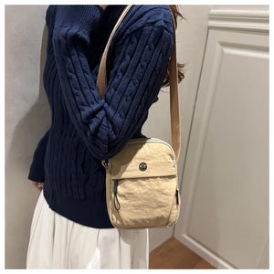 Detail of beige nylon crossbody bag with wide strap worn by a model in a knit sweater