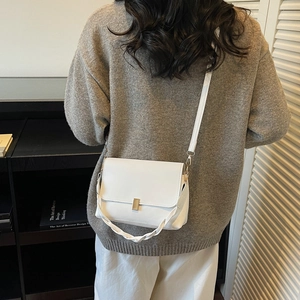 White minimalist square crossbody bag with gold buckle and dual straps on gray sweater