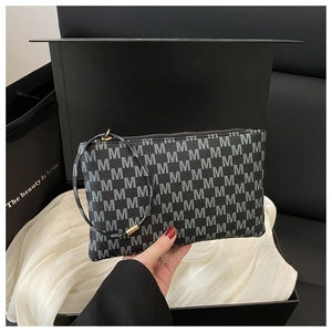Detail of black monogram clutch with M print, round wristlet strap and gold metal hardware