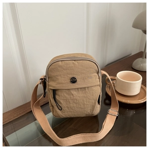 Detail of khaki nylon crossbody bag showing the round M Fashion metal logo and front zipper