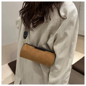 Detailed view of a brown suede cylinder bag with printed strap on white trench coat