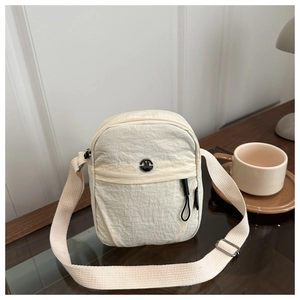 Close-up of cream textured nylon crossbody bag featuring front zipper and fashion metal emblem