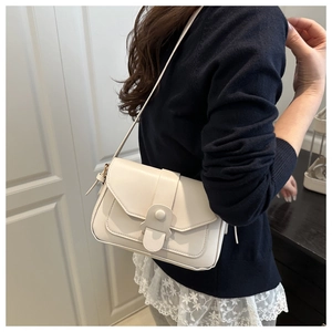 Detail of a minimalist cream flap crossbody bag with decorative buckle on a model