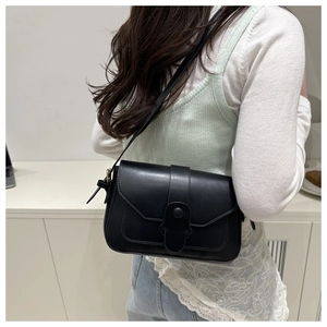 Close-up of a black matte leather square crossbody bag with magnetic closure on a model