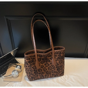 Detail of leopard print tote bag with brown PU straps next to a laptop on a white bed