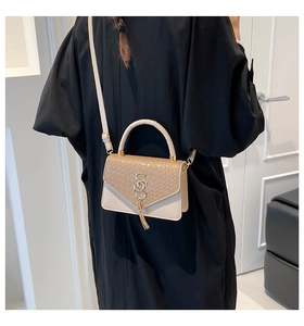 Détail d'un sac à main beige tressé avec pompon et logo métallique porté par le mannequin