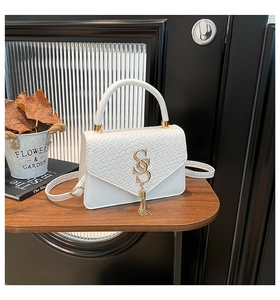 Détail du sac à main blanc à motif crocodile avec logo doré et élégant pompon décoratif