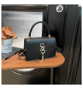 Détail du rabat crocodile noir et cuir mat avec boucle lettre S dorée et pompon