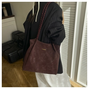 Detail of suede tote bag with braided handle and gold logo on vintage red-brown leather