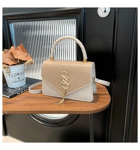 Détail d'un sac bandoulière chic crème et beige avec cuir croco et boucle dorée en S