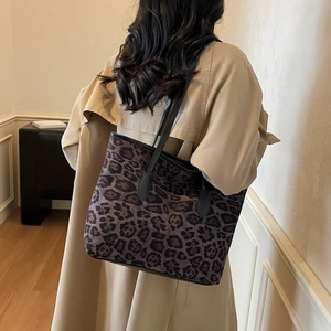 Large leopard print tote bag with black leather straps shown on a model in a warm room