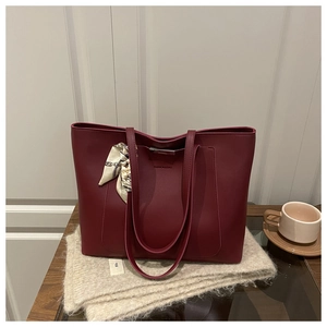 Détail du sac cabas bordeaux avec foulard en soie sur un support en bois élégant