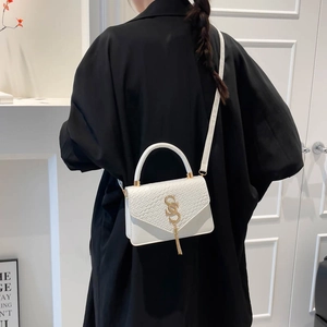 Sac bandoulière blanc motif crocodile avec boucle dorée et pompon porté par un mannequin