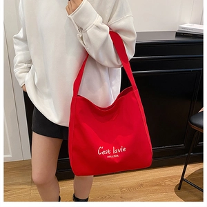 Detail of red canvas tote bag featuring white C'est la vie text and spacious hobo design