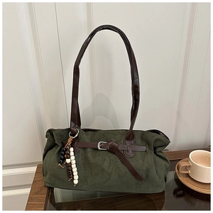 Detail of dark green tote bag featuring a leather buckle strap and beaded charm accessory
