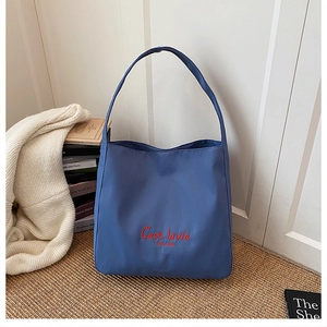 Detail of blue hobo tote bag featuring red C'est la vie embroidery on nylon fabric