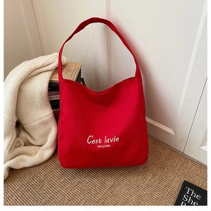 Detail of red canvas tote bag with white C'est lavie text on casual woven mat