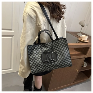 Detail showing high-capacity rectangular tote bag with grey M-letter monogram and leather handle
