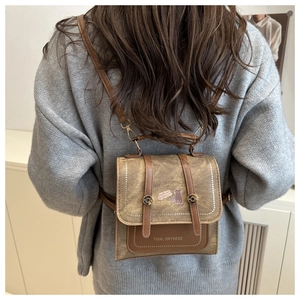 Detailed view of a brown vintage backpack with cat patch on a grey knit sweater