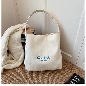Detailed embroidery of C'est lavie on minimalist cream canvas tote bag with wide strap