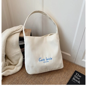 Close-up of cream canvas tote bag with blue 'C'est lavie' embroidery on woven mat