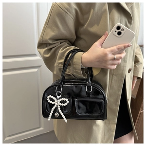 Detail of glossy black patent leather boston bag with pearl bow and heart charm