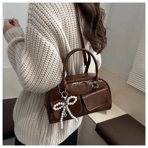 Detail of a shiny dark brown Boston bag featuring side pockets and a pearl bow charm