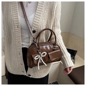 Detail of a brown glossy leather crossbody bag with pearl bow charm and twin front pockets