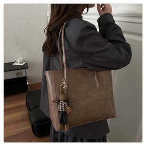 Detail of dark brown leather tote bag with a cute rabbit plush charm in a minimalist interior