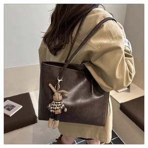 Detail of deep brown vintage matte leather tote bag featuring a cute bunny charm on strap