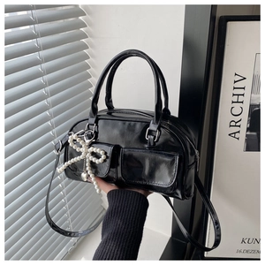 Close-up of a glossy black crossbody bag with twin front pockets and a pearl bow charm