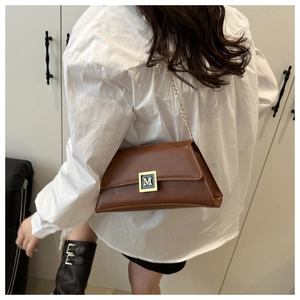 Detail of a brown leather crossbody bag featuring a golden M-shaped metal buckle and chain