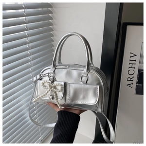 Detailed shot of silver metallic shoulder bag with pearl bow charm and dual front pockets