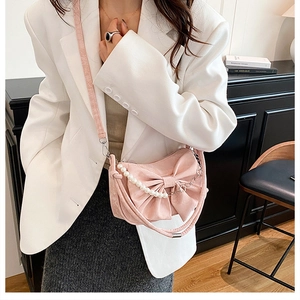 Pink crossbody bag with large bow detail and pearl chain shown on model in white blazer