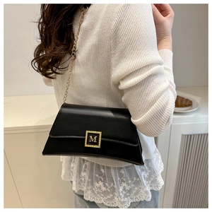 Close-up of minimalist black leather crossbody bag with golden M buckle and chain strap