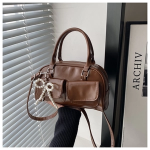 Detail of a brown PU leather shoulder bag with front flap pockets and pearl bow charm