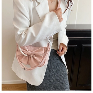 Detailed view of pink satin crossbody bag with large bow and pearl handle on a model