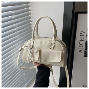 Detail of cream leather crossbody bag featuring pearl bow and heart charm accents