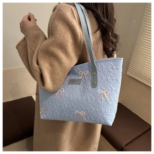 Detail of light blue tote bag featuring quilted texture and pink embroidered bows