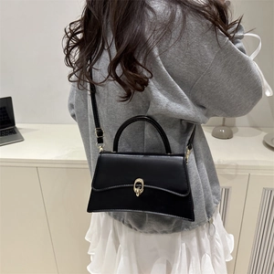 Chic black hourglass crossbody bag with gold buckle on a model in a minimal setting