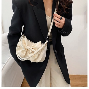 Close-up of beige crossbody bag with large bow detail and pearl chain accessory